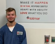 Student apprentice, Dicen, posing in front of a sign at Tolmar.