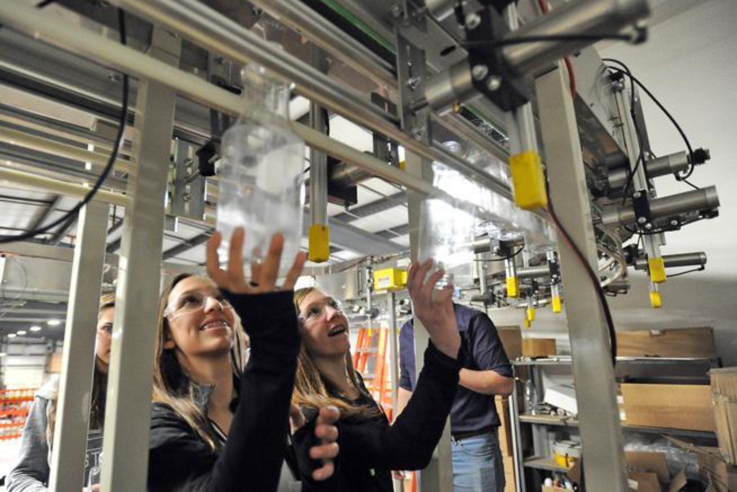 2 Two female youth holding up bottles to an automated machine during a tour at a manufacturing facility.